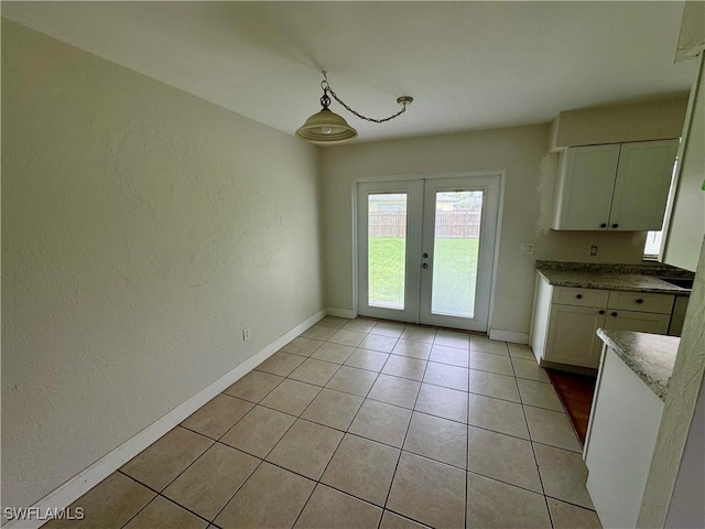 unfurnished dining area with light tile patterned floors, a textured wall, baseboards, and french doors