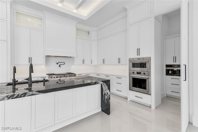 kitchen with appliances with stainless steel finishes, glass insert cabinets, white cabinetry, a sink, and dark stone counters