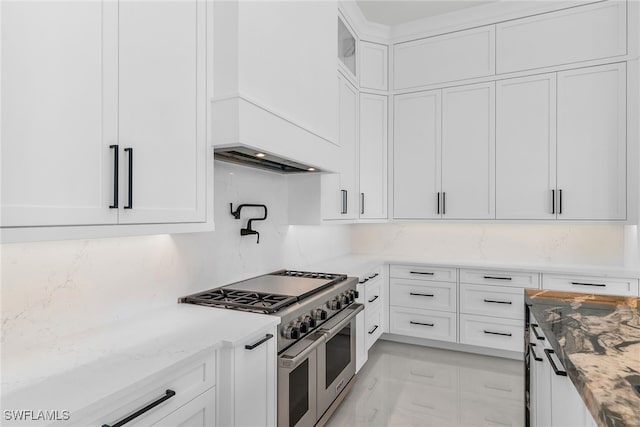 kitchen featuring white cabinets, light stone countertops, range with two ovens, and decorative backsplash