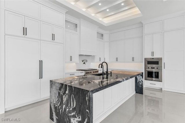 kitchen featuring an island with sink, dark stone countertops, white cabinets, and a sink