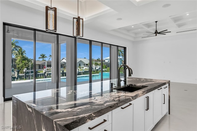 kitchen featuring white cabinets, dark stone counters, coffered ceiling, and a sink