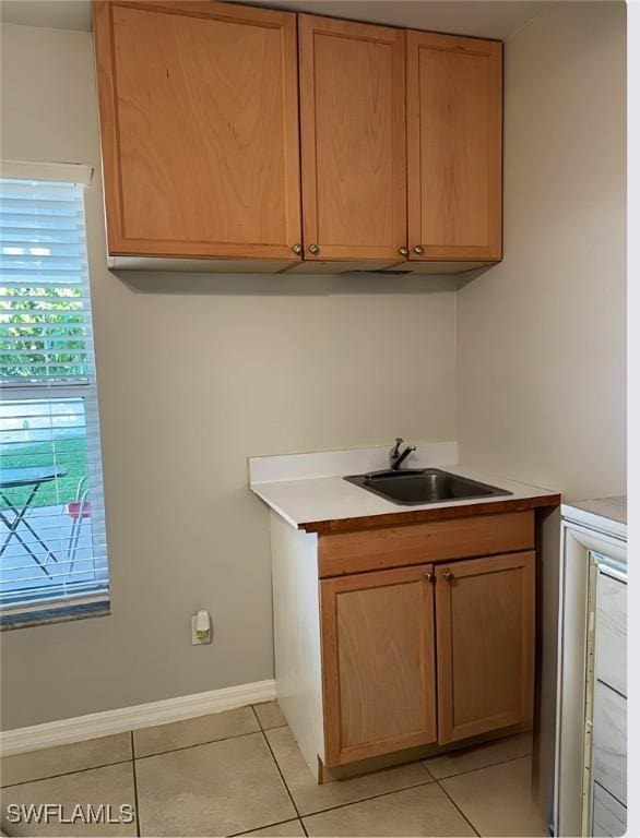 kitchen with light tile patterned floors, baseboards, light countertops, and a sink