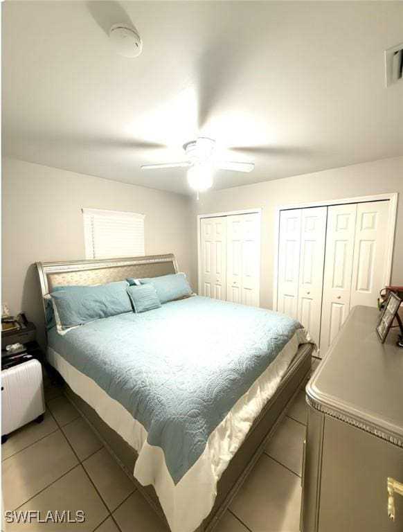 bedroom with ceiling fan, visible vents, multiple closets, and tile patterned floors