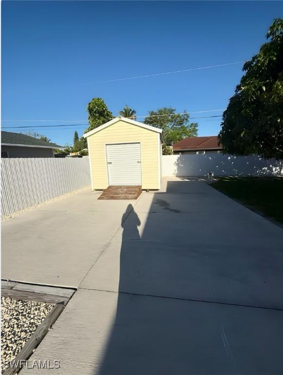 detached garage featuring concrete driveway, fence, and a storage unit