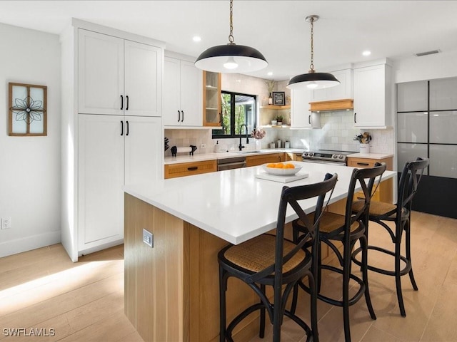 kitchen featuring backsplash, light wood-style flooring, appliances with stainless steel finishes, a kitchen island, and a sink