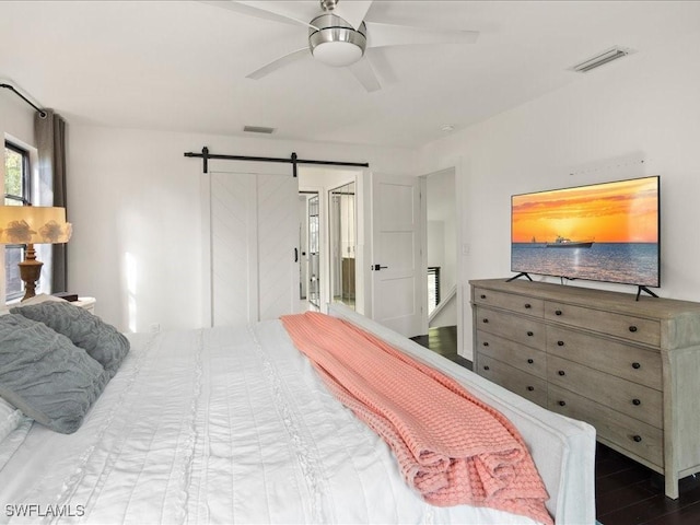 bedroom with a ceiling fan, wood finished floors, visible vents, and a barn door