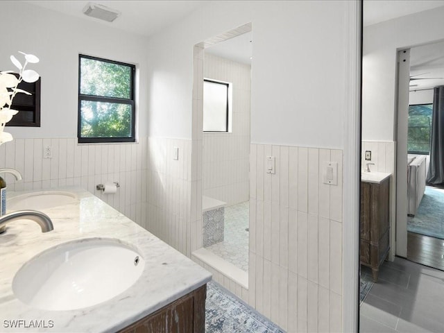 full bath with a walk in shower, double vanity, wainscoting, and a sink