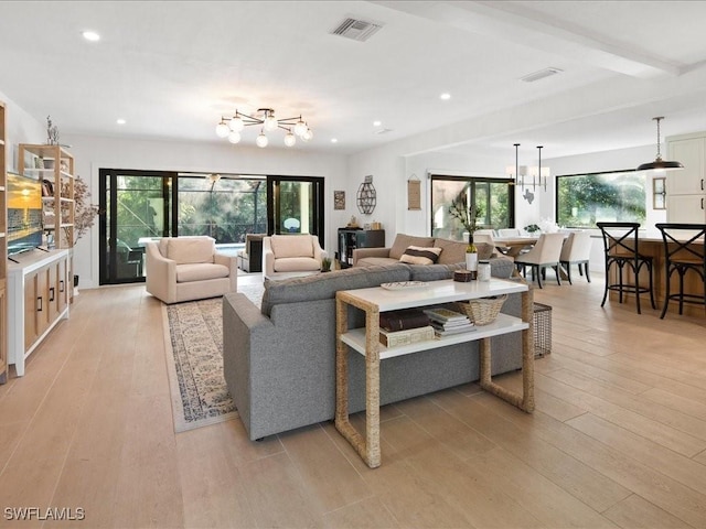 living area featuring light wood finished floors, plenty of natural light, visible vents, and an inviting chandelier