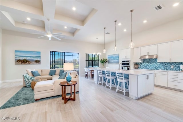 living room featuring visible vents, coffered ceiling, a high ceiling, and ceiling fan