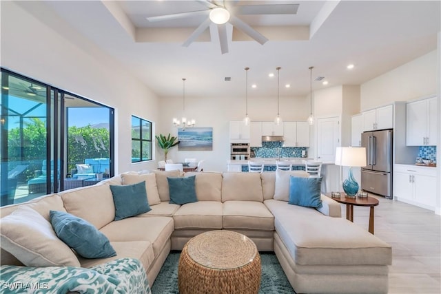 living room with visible vents, ceiling fan with notable chandelier, a tray ceiling, recessed lighting, and a high ceiling