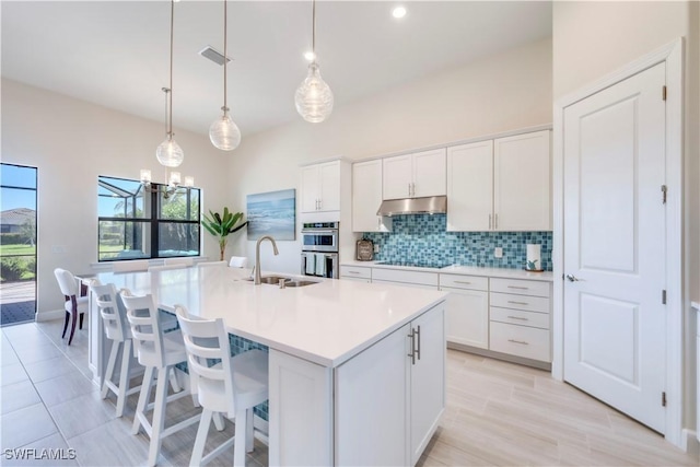 kitchen featuring visible vents, a sink, under cabinet range hood, black electric stovetop, and tasteful backsplash