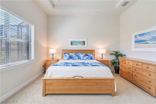 bedroom with visible vents, light carpet, a raised ceiling, and baseboards