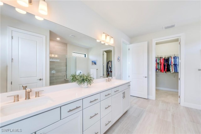 bathroom with a shower stall, a spacious closet, double vanity, and a sink