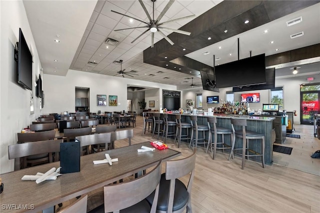 dining space with light wood-type flooring, visible vents, a ceiling fan, and a community bar