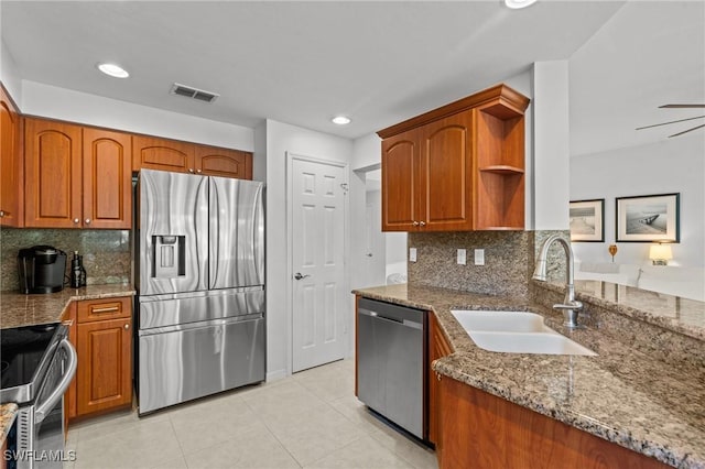 kitchen featuring visible vents, dark stone counters, appliances with stainless steel finishes, brown cabinetry, and a sink