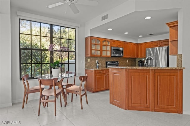 kitchen featuring tasteful backsplash, visible vents, light stone counters, brown cabinets, and appliances with stainless steel finishes