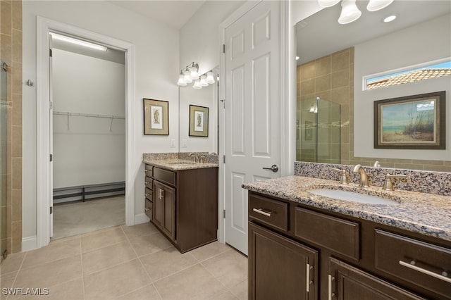 full bath featuring two vanities, a stall shower, a sink, a spacious closet, and tile patterned floors