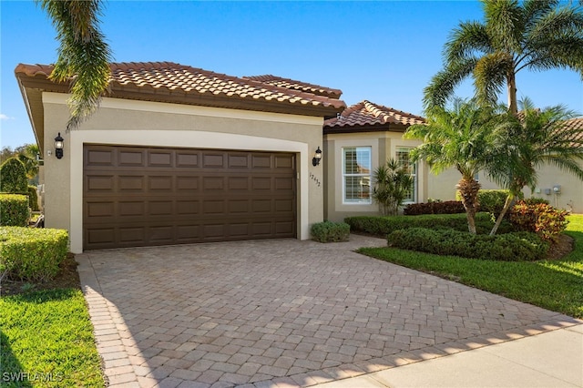 mediterranean / spanish home featuring a tiled roof, stucco siding, an attached garage, and decorative driveway