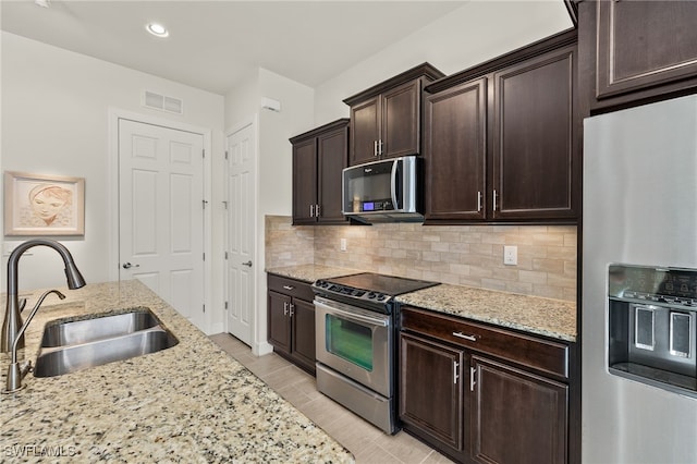 kitchen featuring visible vents, a sink, light stone counters, stainless steel appliances, and decorative backsplash