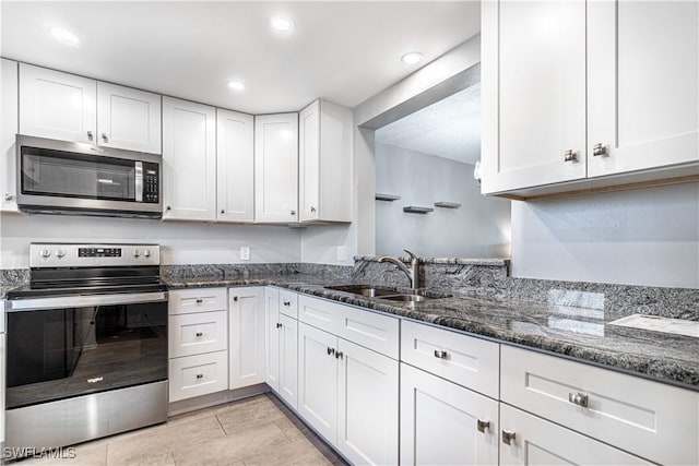 kitchen with recessed lighting, a sink, white cabinetry, appliances with stainless steel finishes, and dark stone countertops