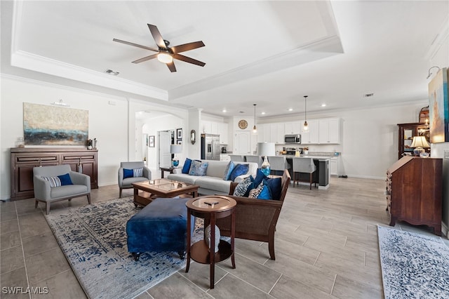 living area featuring a tray ceiling, visible vents, and ornamental molding