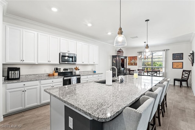 kitchen featuring a center island with sink, a sink, appliances with stainless steel finishes, white cabinets, and crown molding