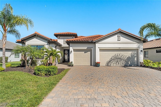 mediterranean / spanish-style house with stucco siding, an attached garage, a tile roof, and decorative driveway