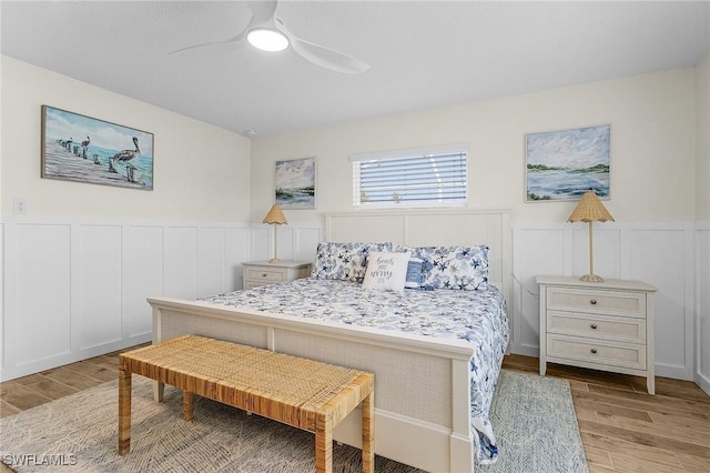 bedroom featuring a wainscoted wall, light wood-style flooring, and a ceiling fan