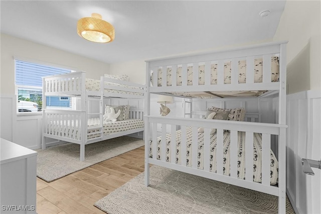 bedroom with a decorative wall, a nursery area, wood finished floors, and a wainscoted wall