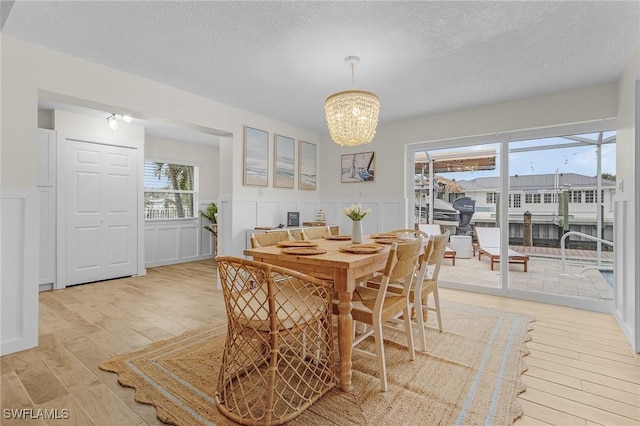 dining area with a wainscoted wall, light wood-style floors, an inviting chandelier, and a textured ceiling