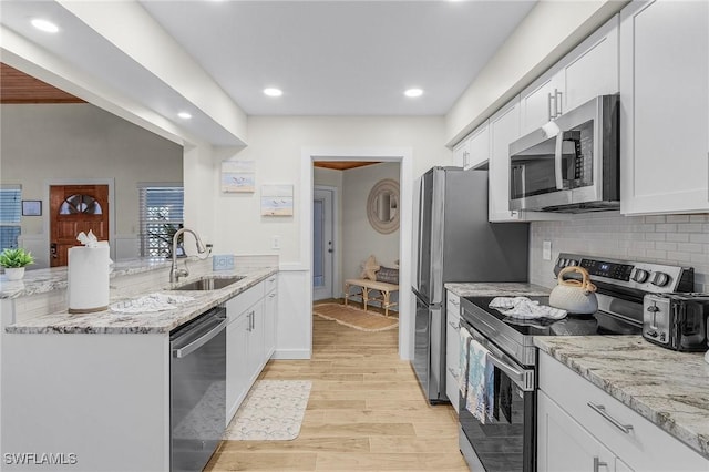 kitchen with light wood-type flooring, a peninsula, stainless steel appliances, white cabinetry, and a sink