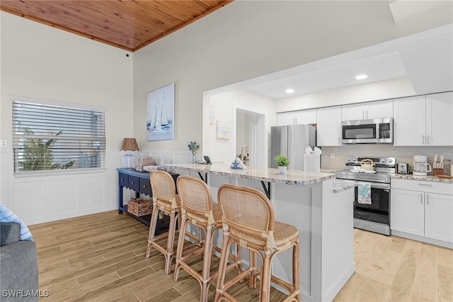 kitchen with a kitchen breakfast bar, light wood finished floors, light stone countertops, and appliances with stainless steel finishes