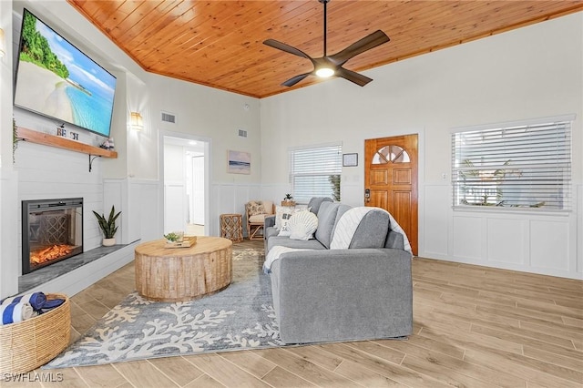 living area featuring a decorative wall, wooden ceiling, a large fireplace, and light wood-style floors