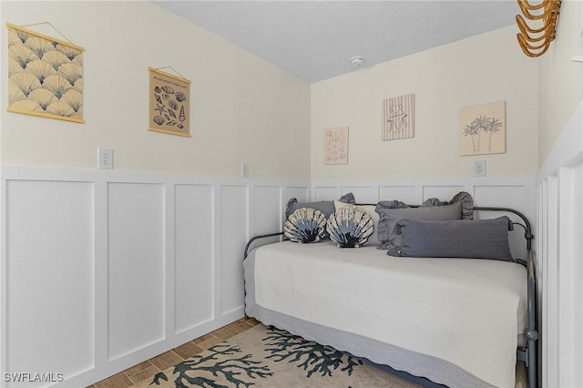 bedroom with a decorative wall, wainscoting, and light wood-type flooring