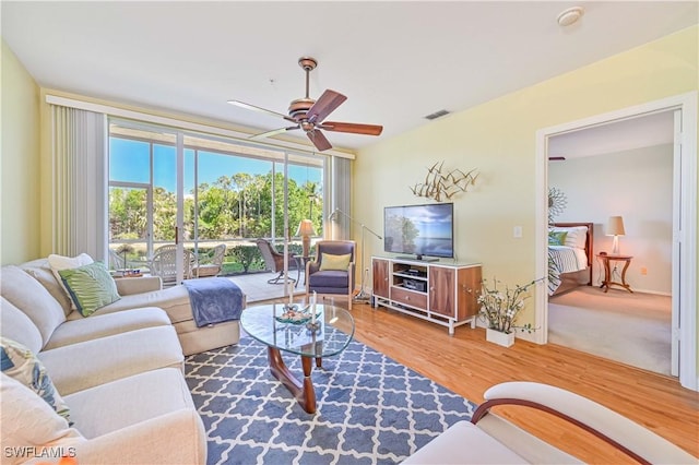 living room featuring a wall of windows, visible vents, ceiling fan, and wood finished floors