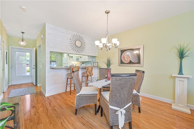 dining area featuring baseboards, light wood finished floors, and an inviting chandelier