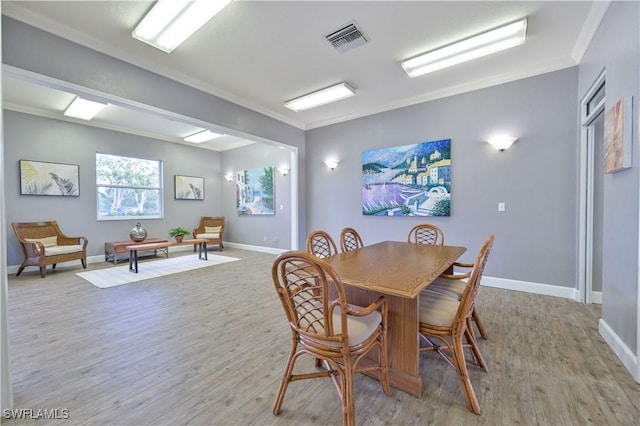 dining room featuring ornamental molding, light wood-type flooring, visible vents, and baseboards