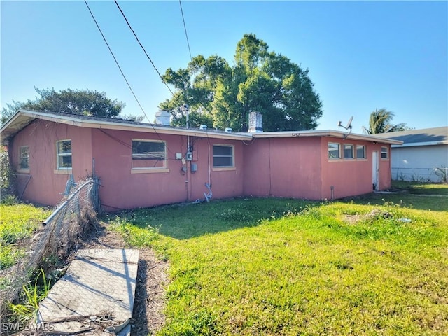 rear view of property with a yard, fence, and stucco siding