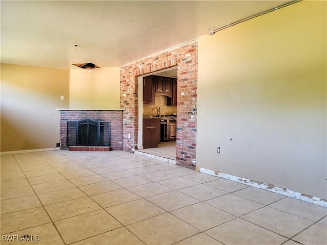 unfurnished living room with a brick fireplace, light tile patterned flooring, a sink, and baseboards