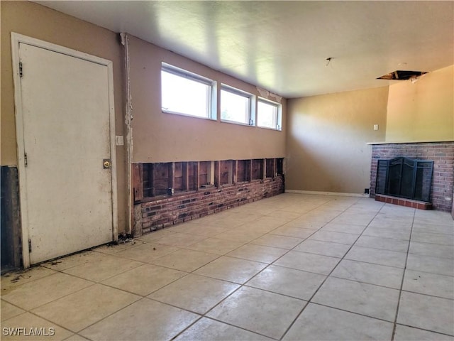 unfurnished living room with a brick fireplace, brick wall, and tile patterned floors