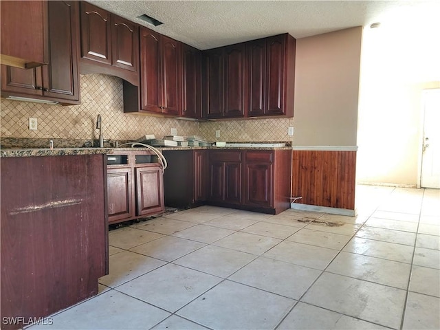 kitchen featuring tasteful backsplash, dark stone countertops, a textured ceiling, a sink, and light tile patterned flooring