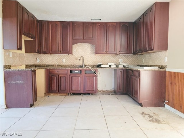 kitchen featuring reddish brown cabinets, stone counters, tasteful backsplash, light tile patterned flooring, and a sink