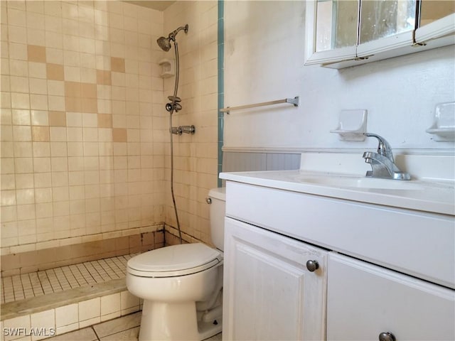 bathroom with tiled shower, tile patterned flooring, vanity, and toilet