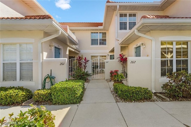 doorway to property with a tiled roof, fence, a gate, and stucco siding