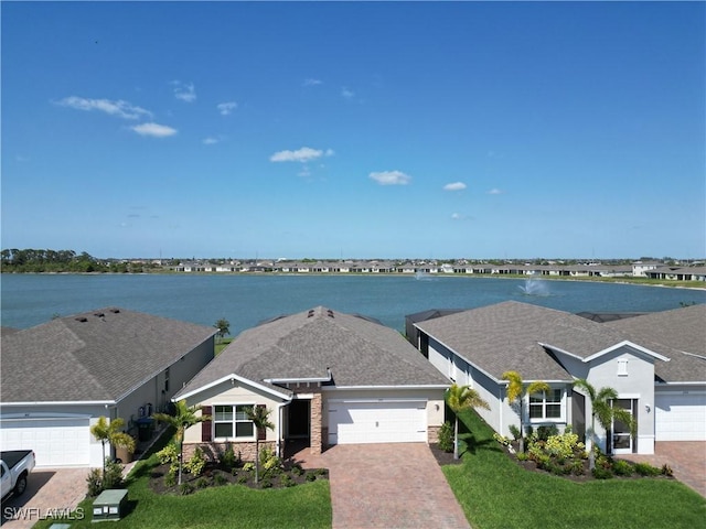 view of front facade with decorative driveway, a water view, an attached garage, a front yard, and stone siding