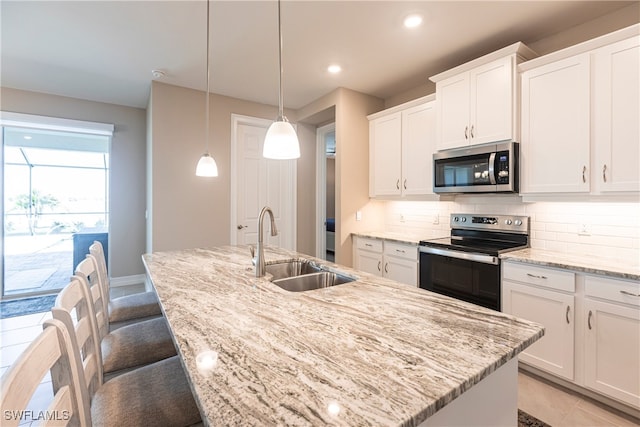 kitchen with a center island with sink, white cabinets, decorative backsplash, appliances with stainless steel finishes, and a sink