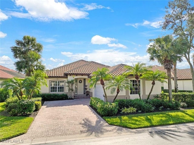 mediterranean / spanish home featuring stucco siding, decorative driveway, an attached garage, and a tiled roof