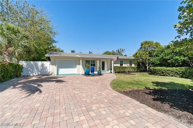 ranch-style home featuring decorative driveway, a front yard, an attached garage, and fence