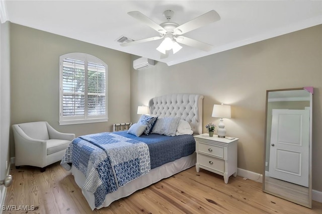 bedroom with a wall unit AC, light wood finished floors, baseboards, and visible vents