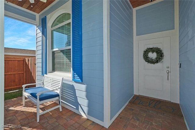 view of exterior entry with ceiling fan, fence, and a porch